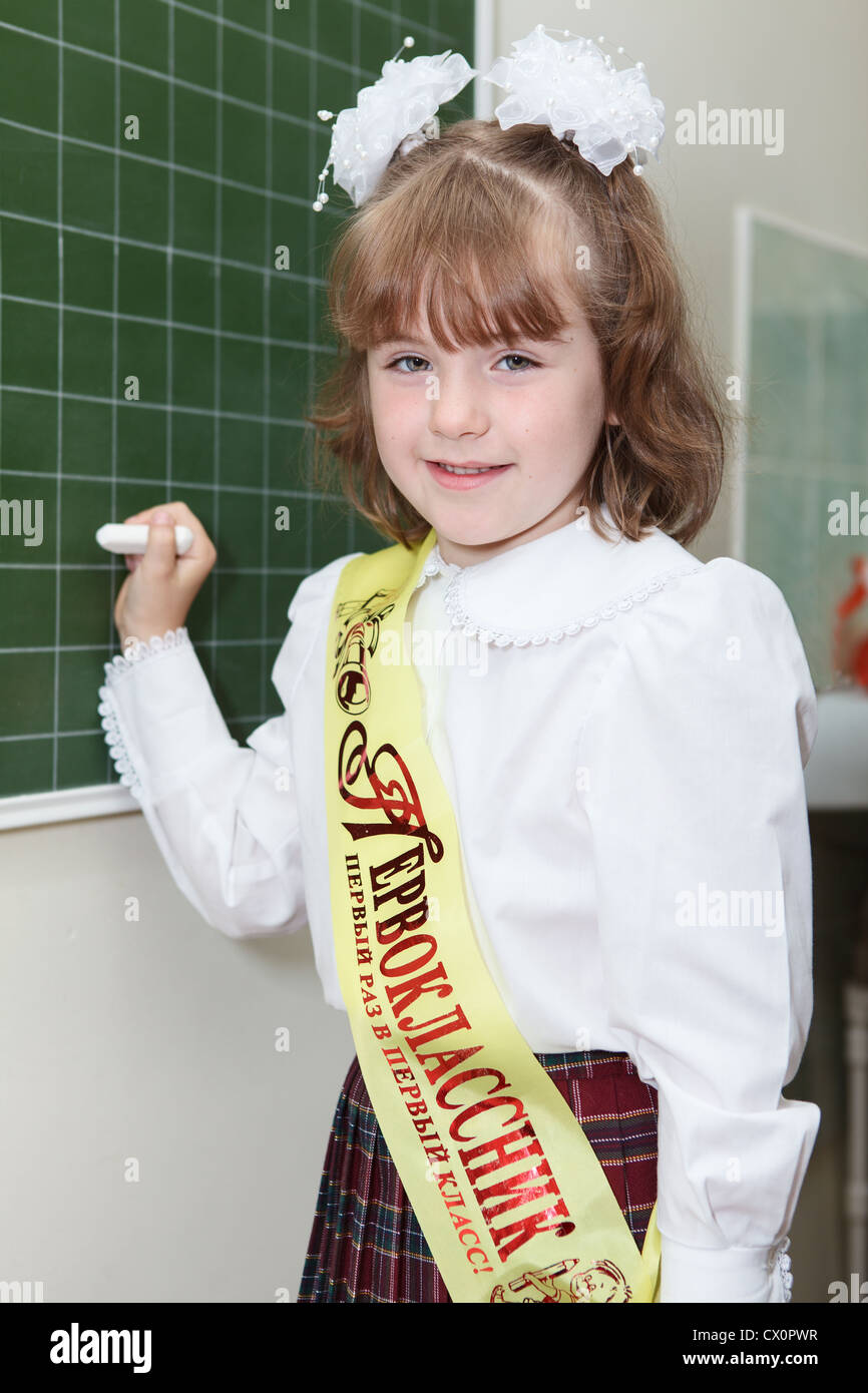 Piccola ragazza di un allievo di prima classe della scuola elementare in piedi dietro una lavagna con Chalk Foto Stock