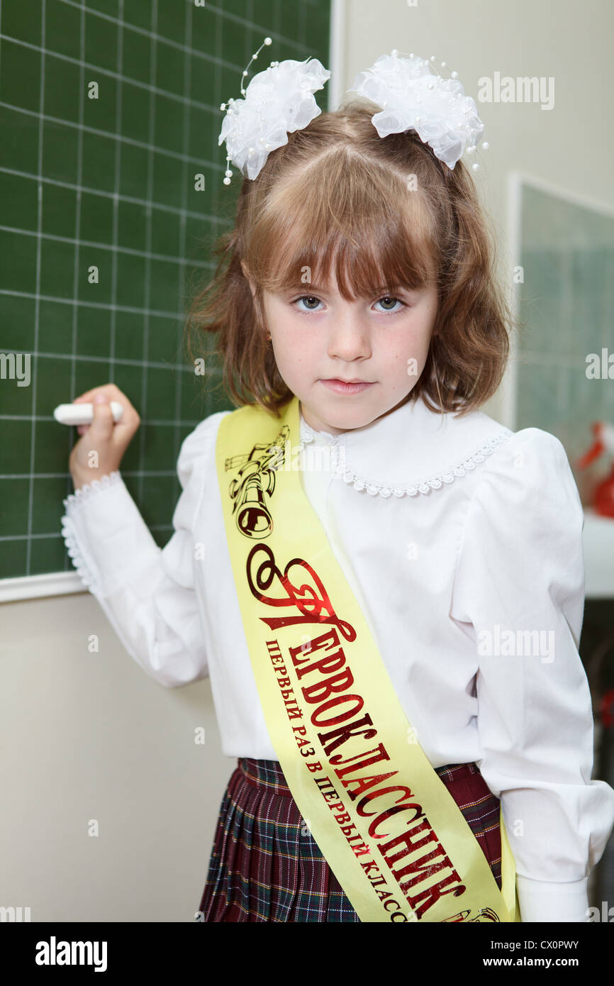 Piccola ragazza russa di un allievo di prima classe della scuola elementare in piedi dietro una lavagna verde con Chalk Foto Stock