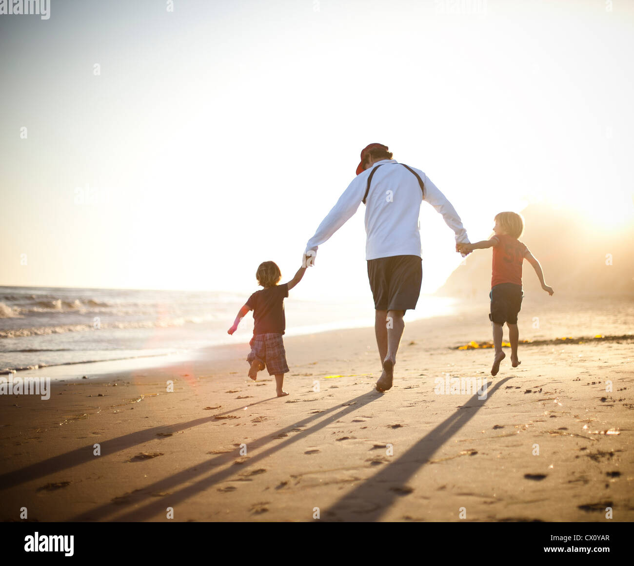 Padre e figli camminando mano nella mano sulla spiaggia al tramonto