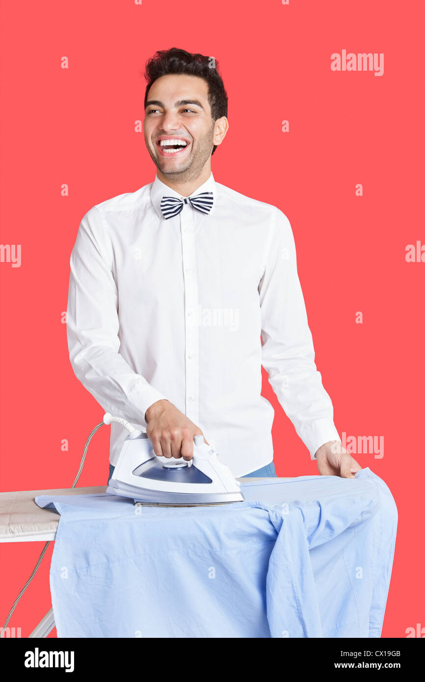 Uomo sorridente in formali la stiratura camicia su sfondo rosso Foto Stock