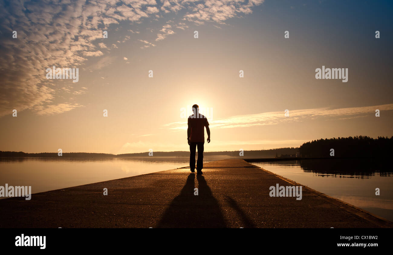 Un uomo passa sul molo di cemento nel sunrise Foto Stock