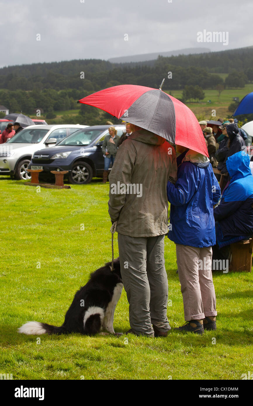 Cane, l uomo e la donna il ricovero sotto ombrellone al Threlkeld Show, Threlkeld, Keswick, Lake District, Cumbria, England, Regno Unito Foto Stock