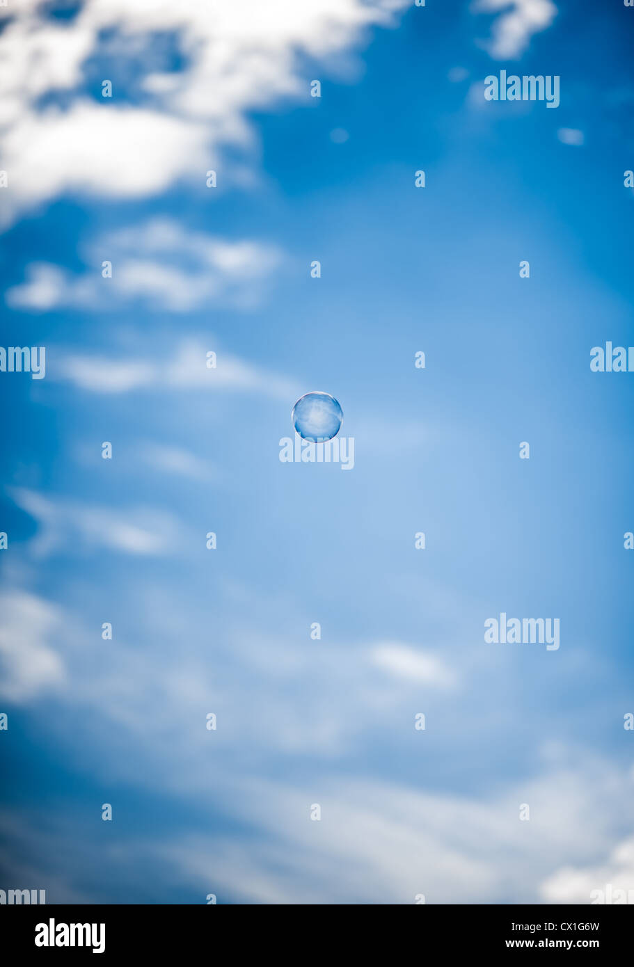 Una sferica singola bolla di sapone, appena sopra il centro, galleggia in un profondo cielo blu con nuvole sfocati sopra. Foto Stock