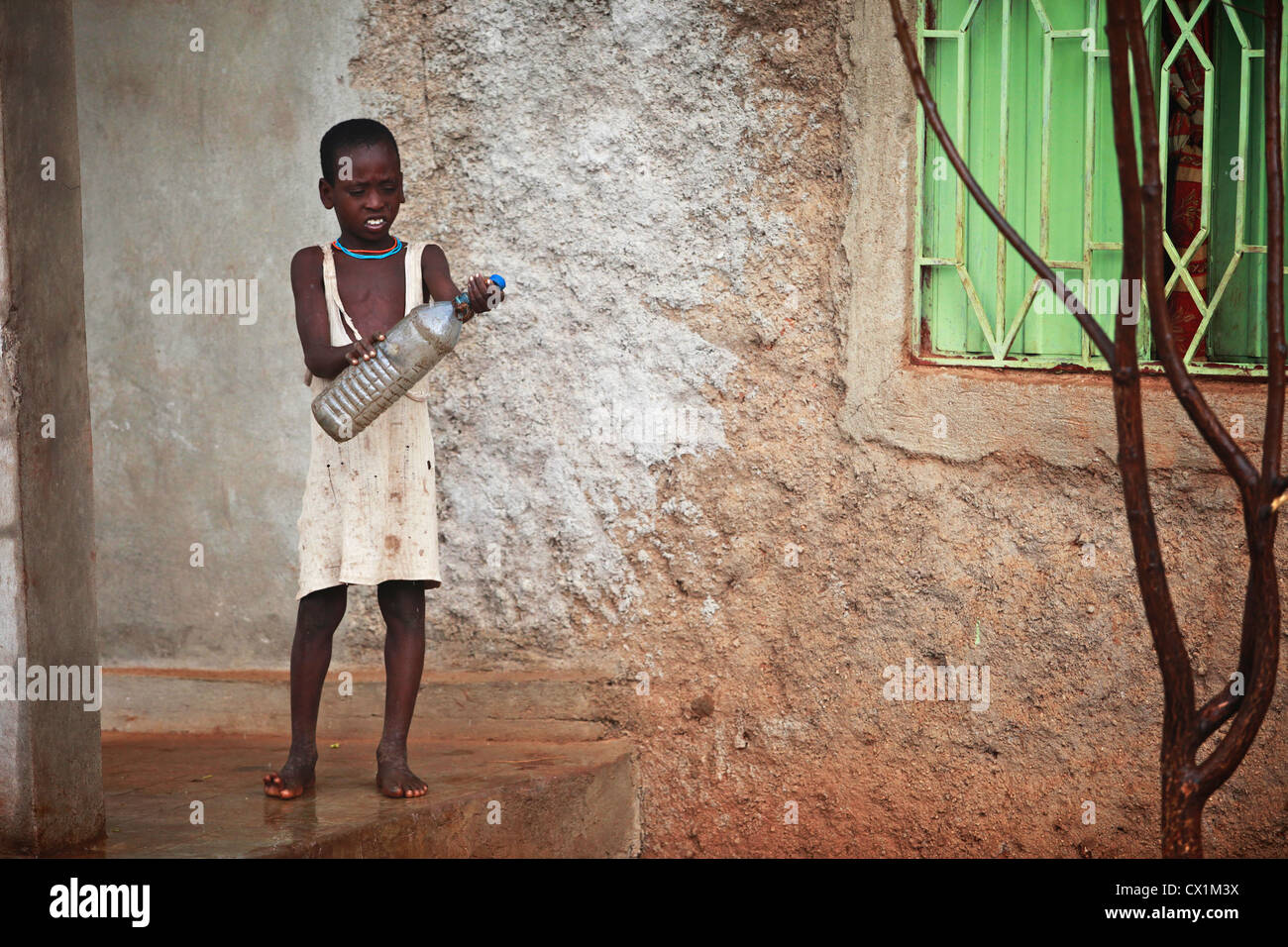 Un giovane bambino cercando di raccogliere eventuali gocce di pioggia in una bottiglia vuota. Foto Stock
