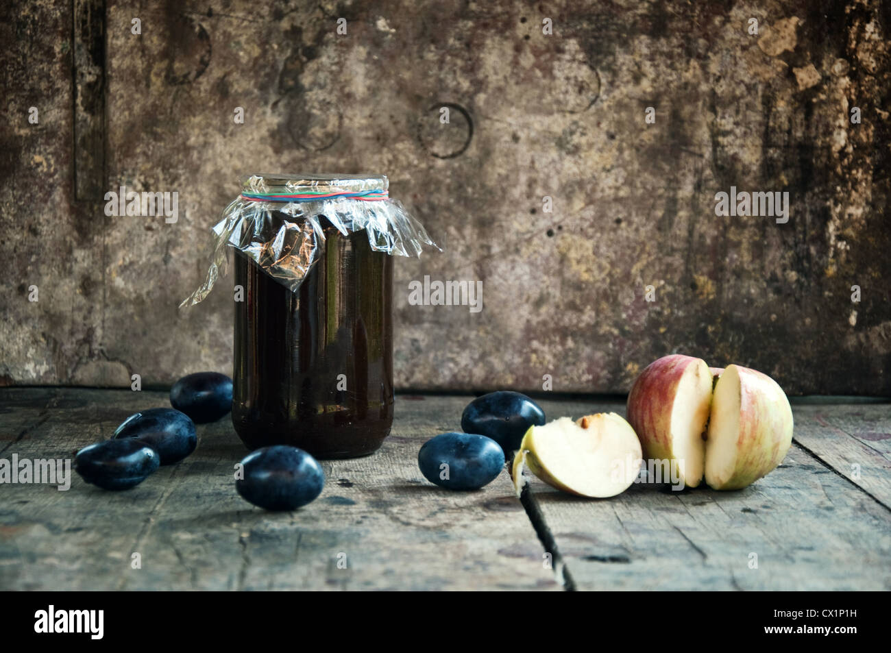 Un vasetto di marmellata di prugne su un tavolo di legno con alcune Prugne e un apple, la produzione di alimenti biologici Foto Stock