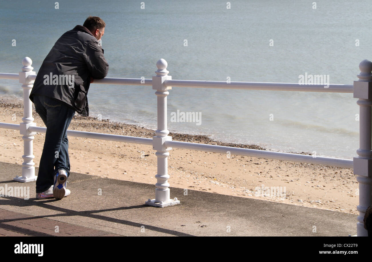 Uomo appoggiato sulle ringhiere sul fronte mare. Foto Stock