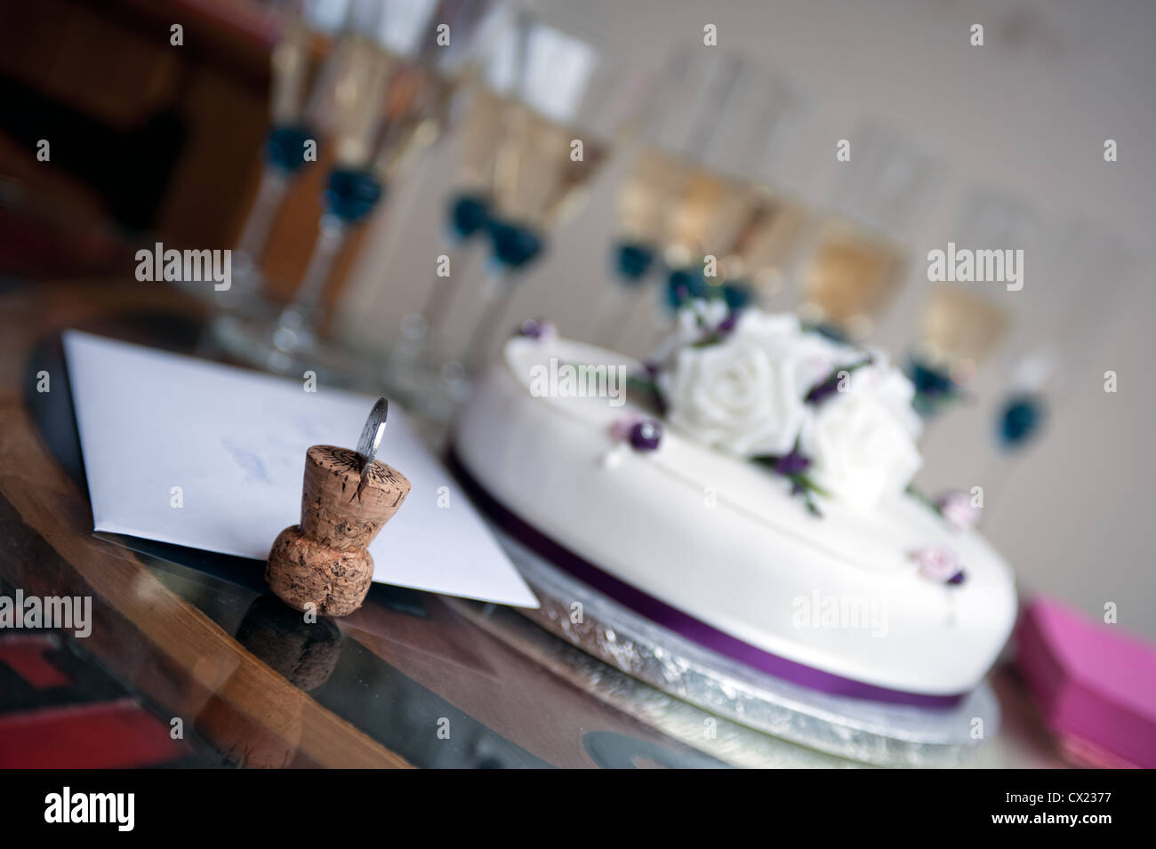 Tappo dello Champagne con moneta inserita contro lo sfondo di una torta nuziale e champagne Foto Stock