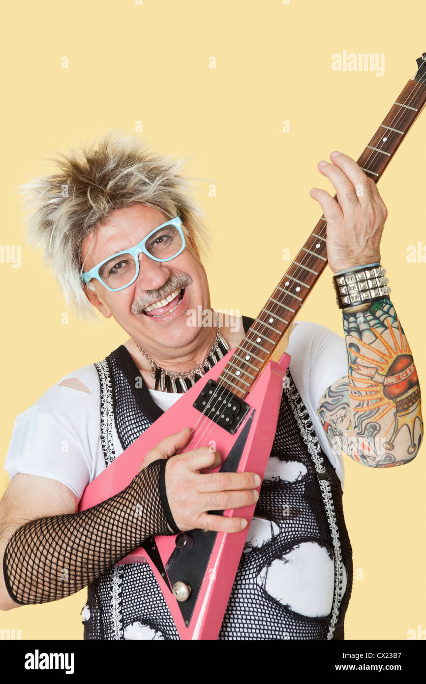 Ritratto di felice maschio senior punk rock musicista suonando la chitarra su sfondo giallo Foto Stock