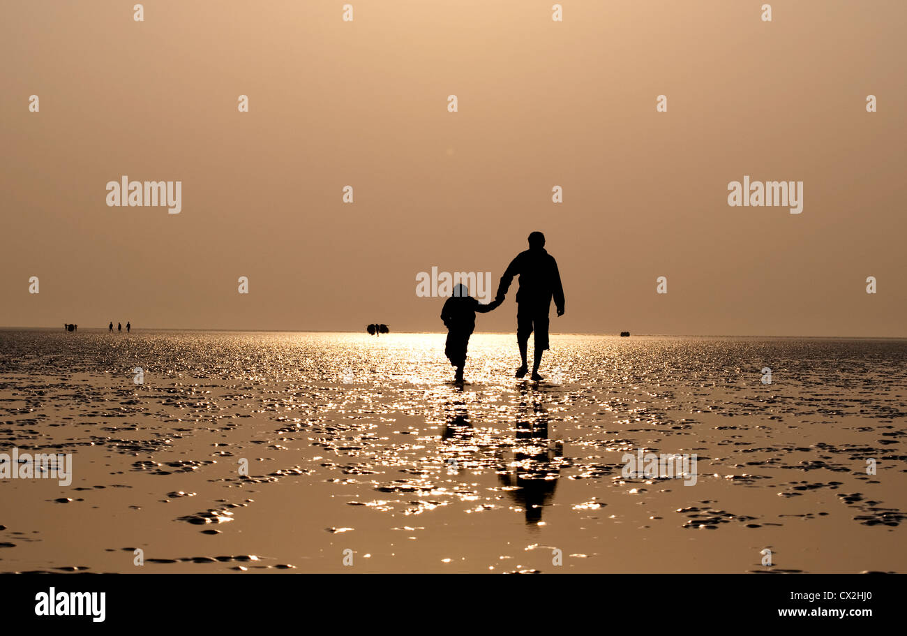 Bambino cammina con suo padre sulla spiaggia di mare a Chandipur, Orissa, India. Foto Stock