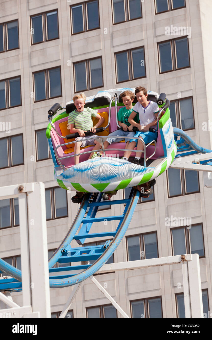 3 persone nella cabina di un roller coaster circa per effettuare una rapida discesa. Dietro la cabina è un edificio con un sacco di windows. Foto Stock