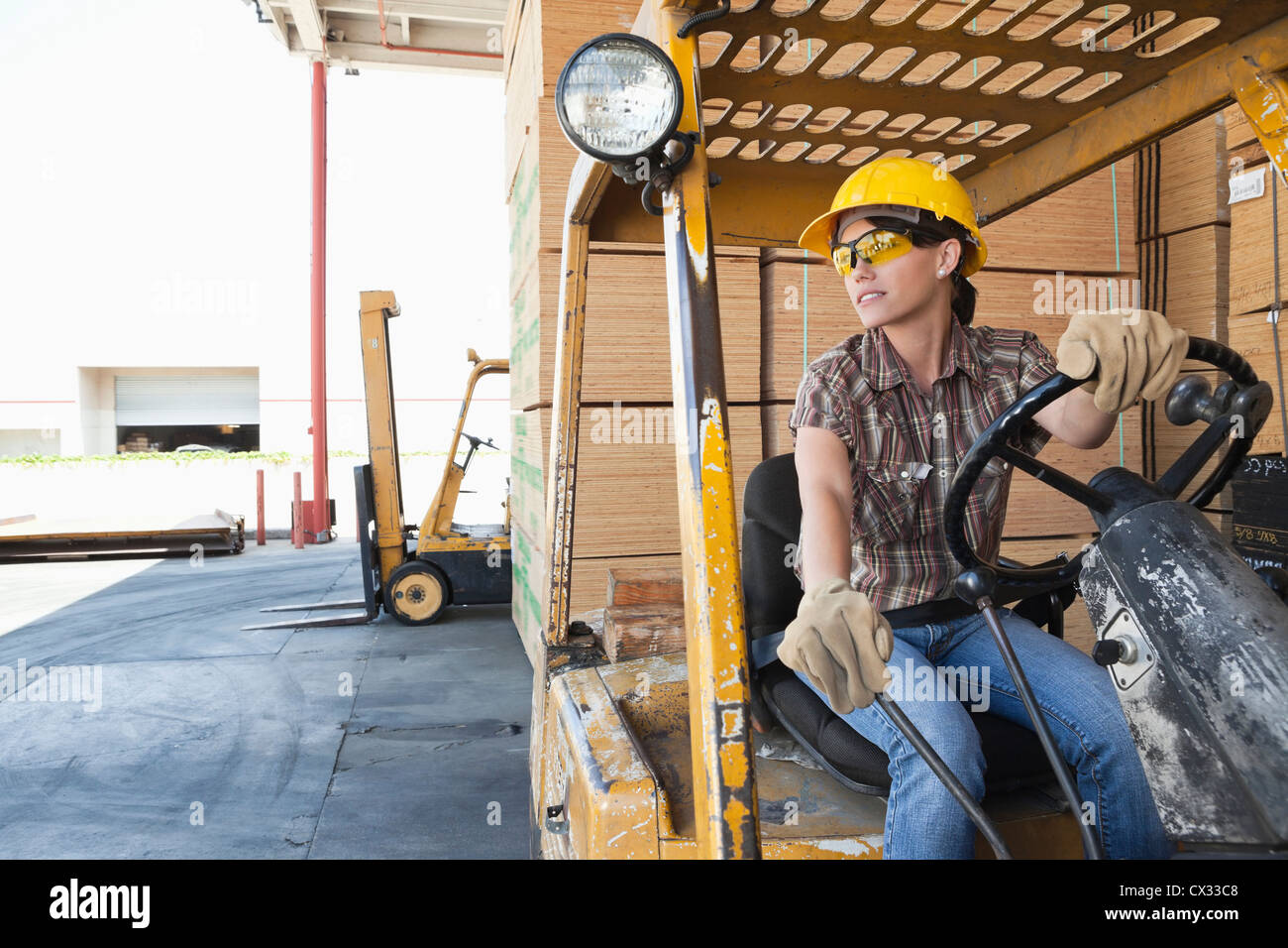 Femmina lavoratore industriale che guarda lontano mentre si guida il carrello elevatore Foto Stock