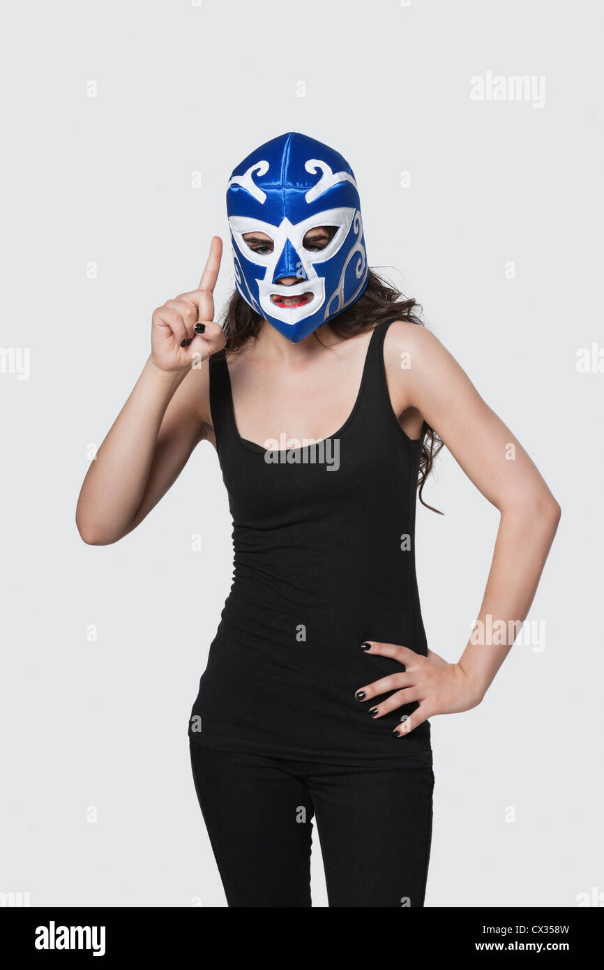 Giovane donna che indossa la maschera di wrestling come lei solleva il dito indice contro uno sfondo grigio Foto Stock