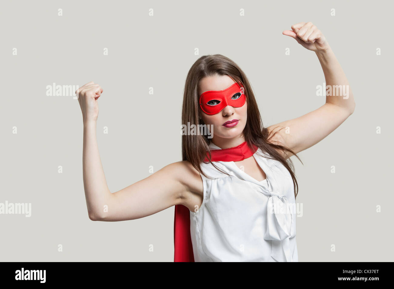 Ritratto di una giovane donna in super hero costume i muscoli di flessione su sfondo grigio Foto Stock