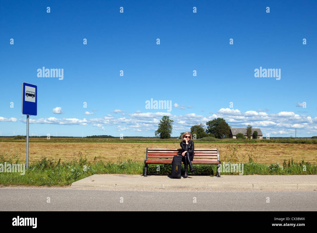 Lonely donna seduta su una panchina alla fermata del bus in campagna Foto Stock