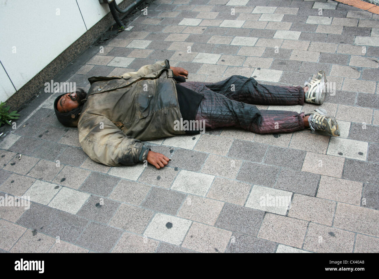 Un senzatetto giacente in stato di incoscienza in strada. Foto Stock
