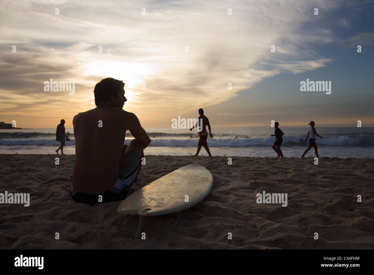 Uomo seduto sulla spiaggia con la tavola da surf. La spiaggia di Bondi, Sydney, Nuovo Galles del Sud, Australia Foto Stock
