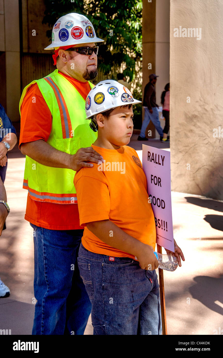 Indossa il suo colorato di apparecchiature di sicurezza, un padre ispanica porta il suo figlio in un raduno nonviolenta di costruzione locale dei lavoratori. Foto Stock