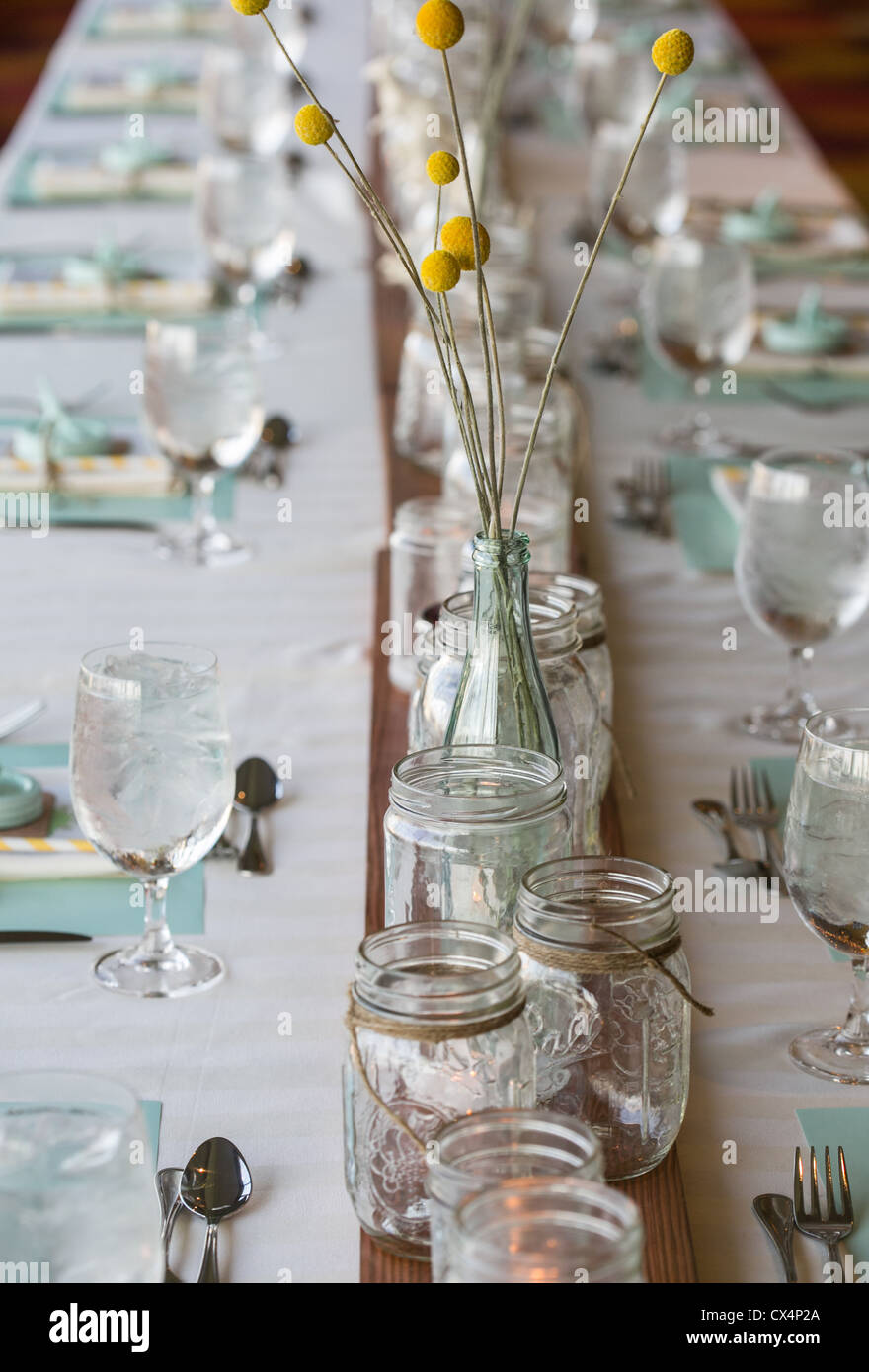 Tavolo rustico impostazione per un matrimonio con vasetti di vetro Bottiglie di vetro azienda Craspedia (Billy sfere) Fiori Foto Stock