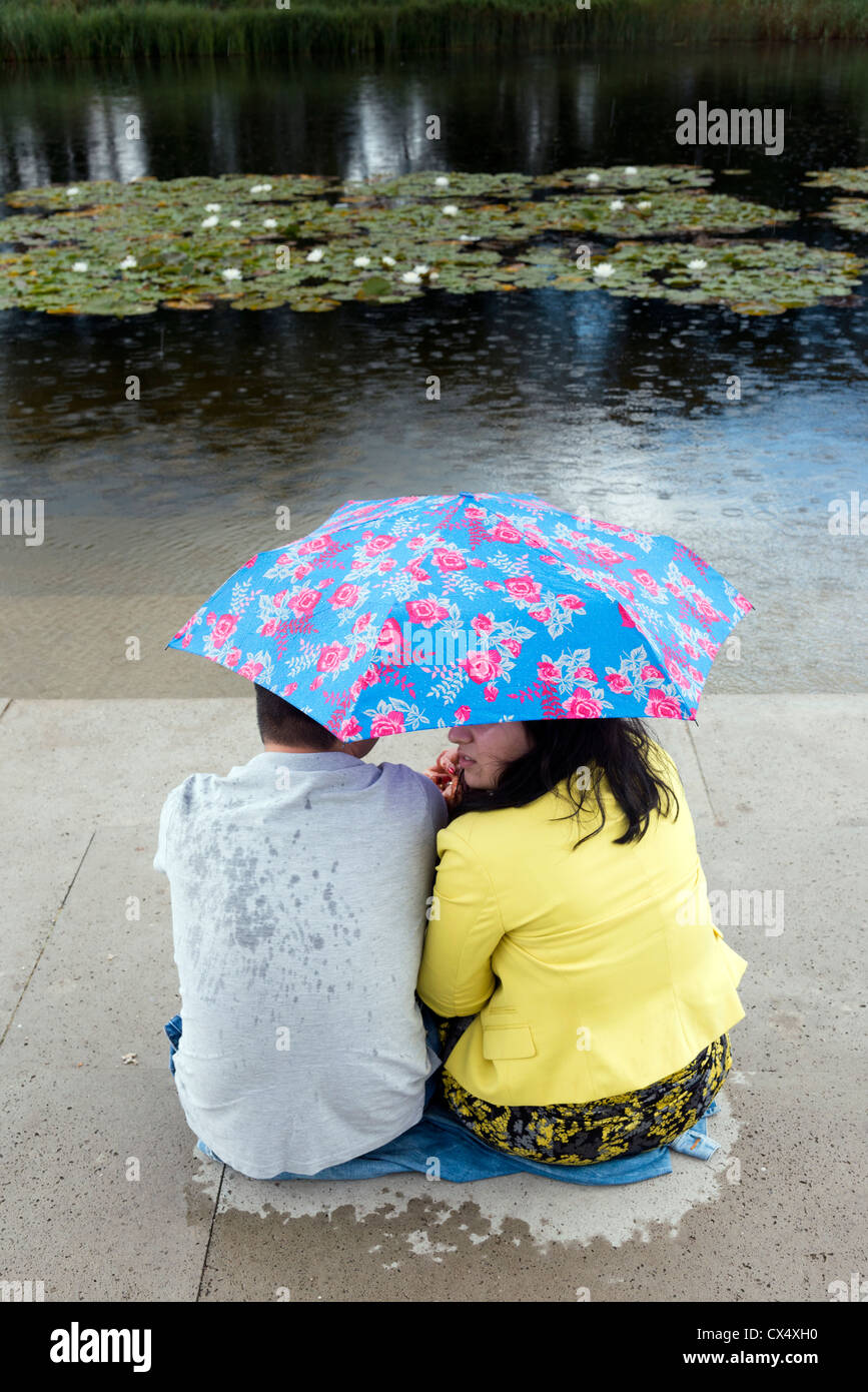 Accoppiare il ricovero sotto un ombrello durante la pioggia sul lato di un lago a Floriade 2012 World Horticultural Expo Venlo Paesi Bassi Foto Stock