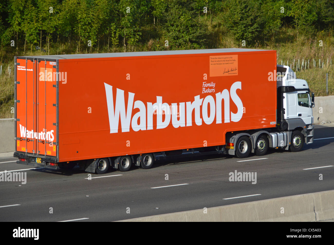 I dettagli aziendali della panetteria di proprietà della famiglia Warburtons pubblicizzati sul lato della catena di fornitura del pane camion e rimorchio che guida lungo l'autostrada M25 UK Foto Stock