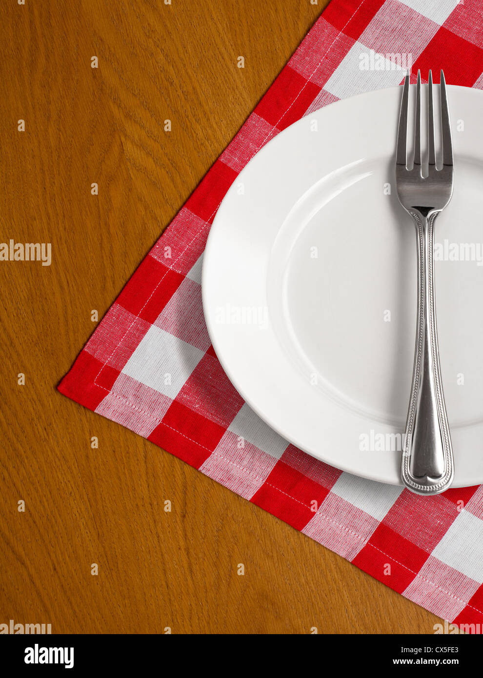 Piastra bianca e forcella su un tavolo di legno con rosso tovaglia controllati Foto Stock