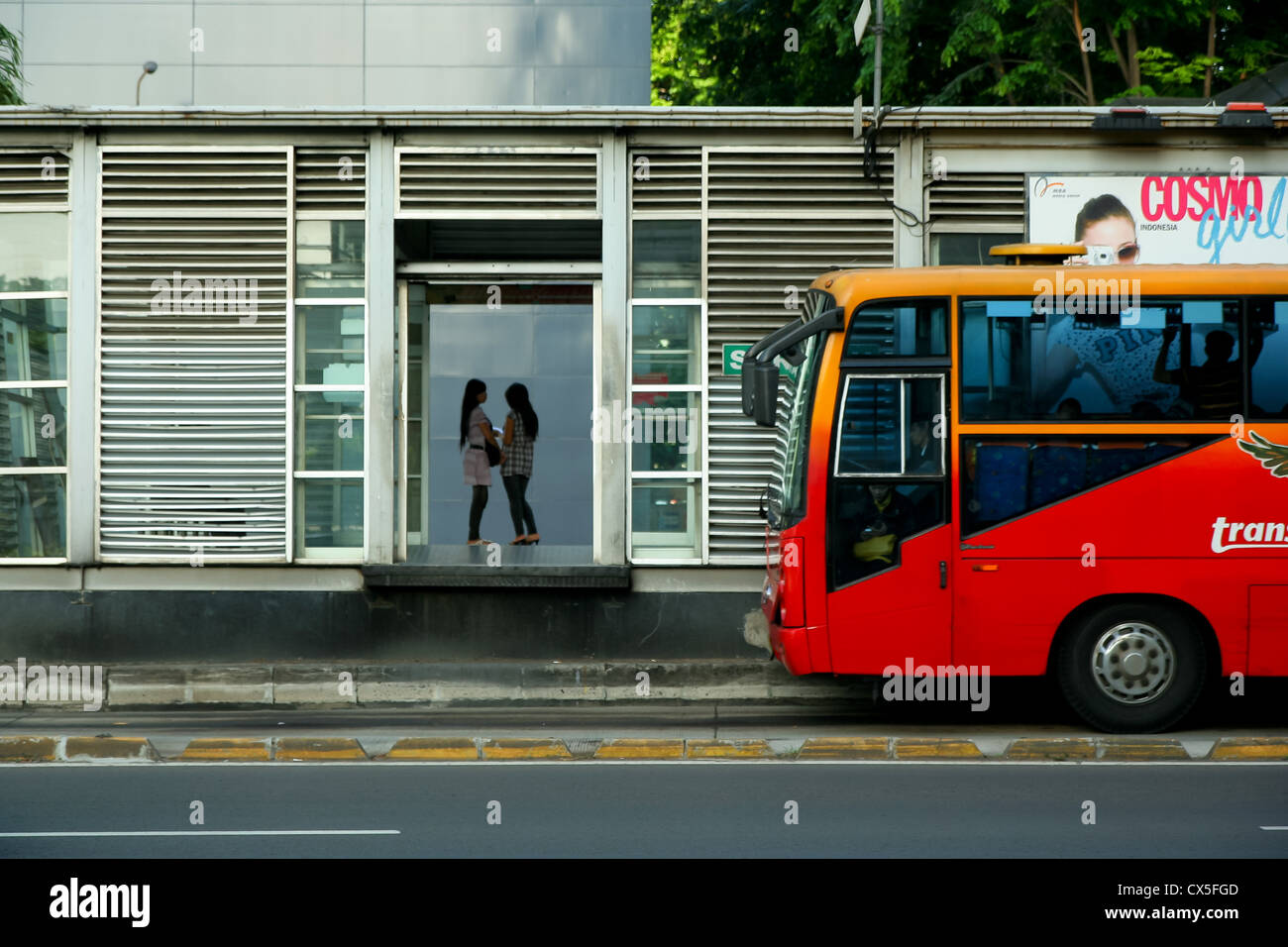 Due donne in attesa di un bus Trans-Jakarta che sta arrivando. Foto Stock