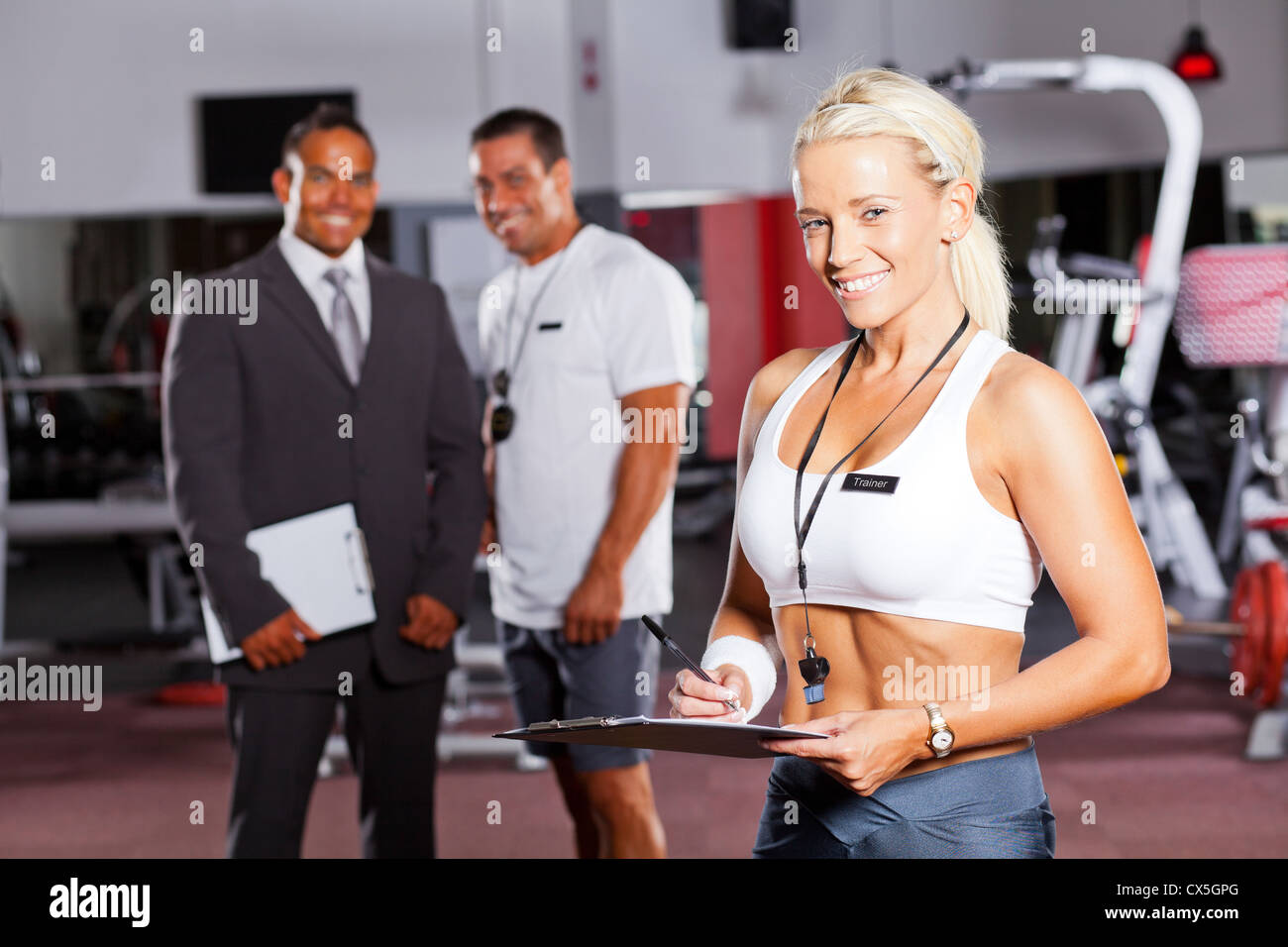 Felice palestra femmina trainer ritratto con i colleghi in background Foto Stock