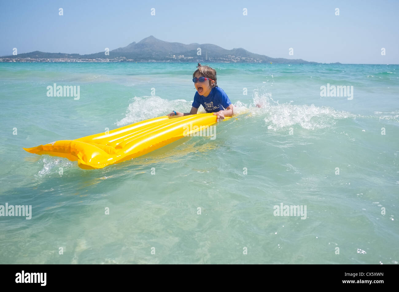 Un giovane ragazzo divertendosi nel surf su una zattera gonfiabile lilo Foto Stock
