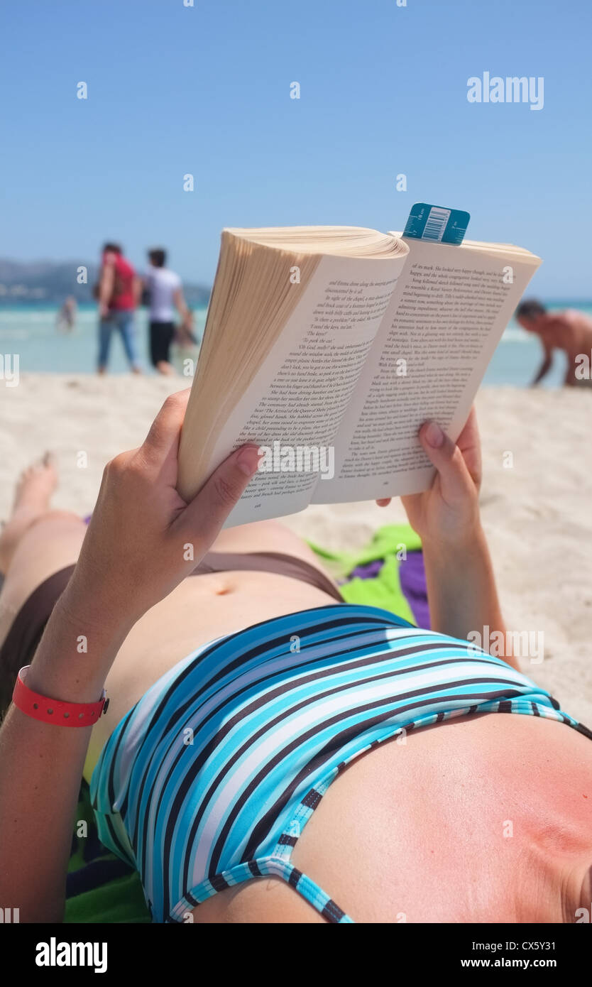 Una lettura di donne vacanza prenotare sulla spiaggia mentre il sole Foto Stock