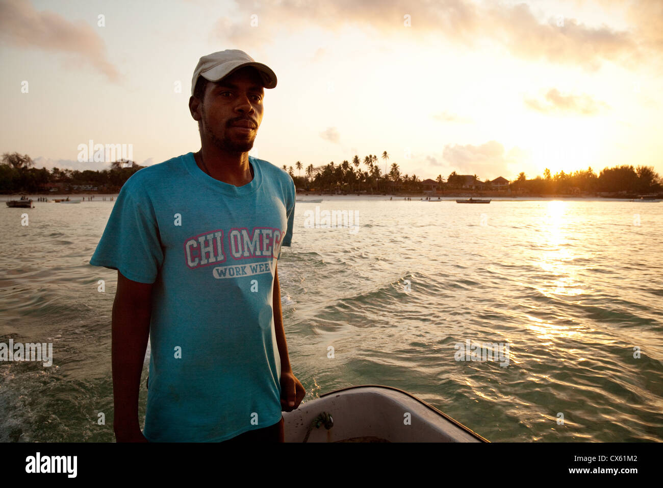 Un Zanzibari uomo africano lo sterzo la sua barca sull'Oceano Indiano a sunrise per andare a osservare i delfini, Zanzibar Africa Foto Stock