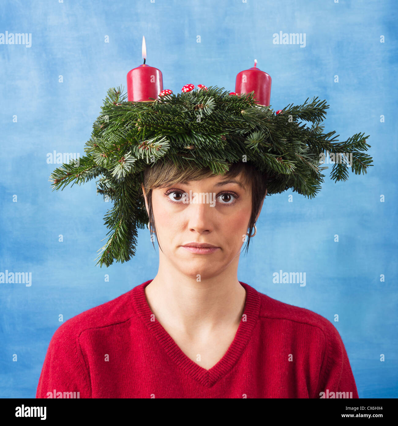 Triste giovane donna indossa corona di Avvento sulla sua testa una candela brucia, xmas studio shot contro un blu e sfondo bianco Foto Stock