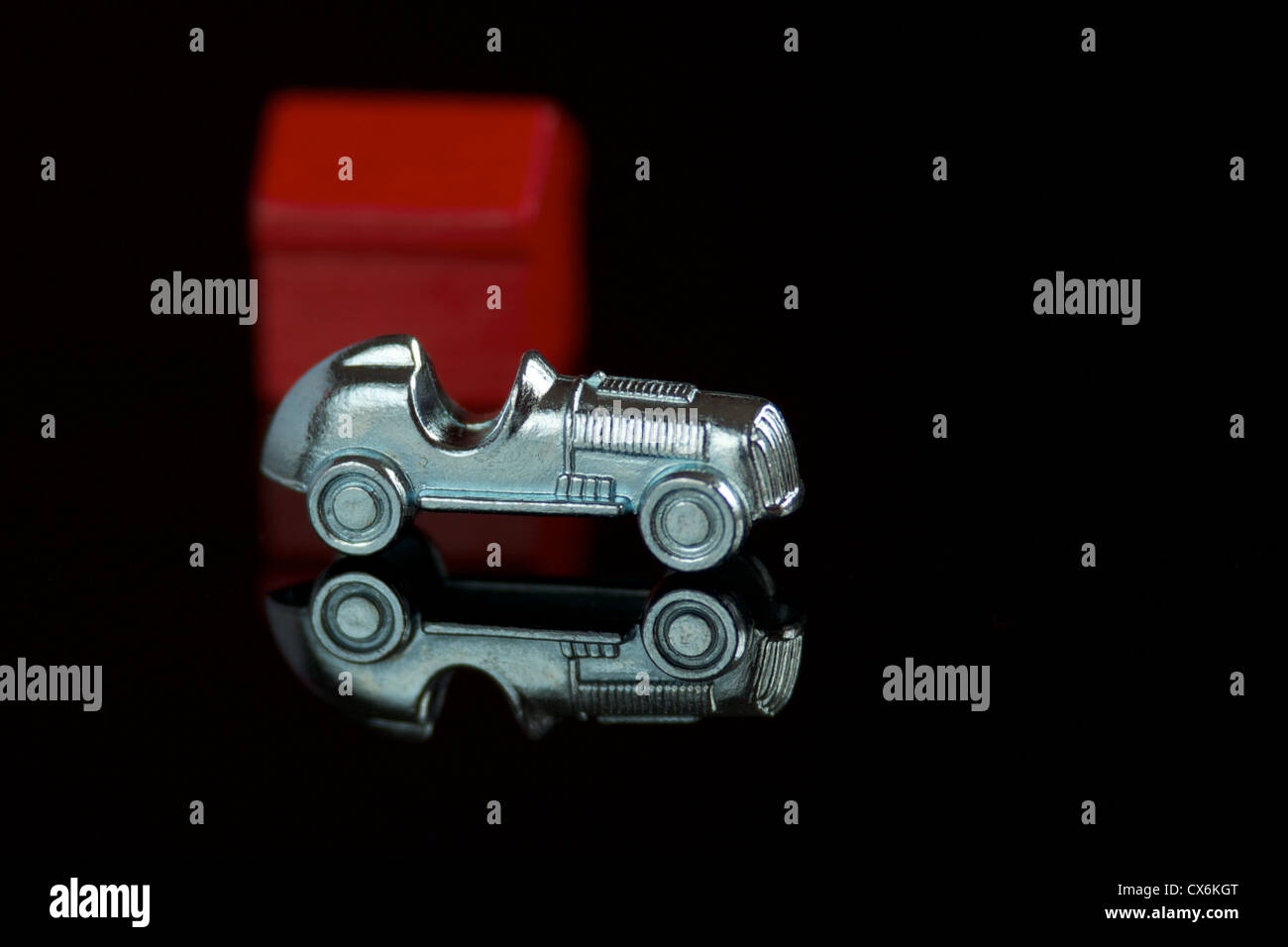 Monopolio gioco auto pezzo nella parte anteriore di un rosso di legno casa isolata su uno sfondo nero con la riflessione Foto Stock