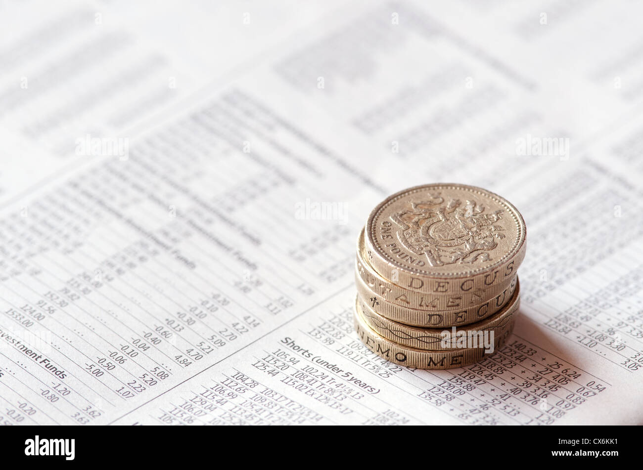 Pila di monete Britanniche seduti sul giornale che mostra i prezzi dei fondi di investimento. Focus sulla faccia della moneta superiore Foto Stock