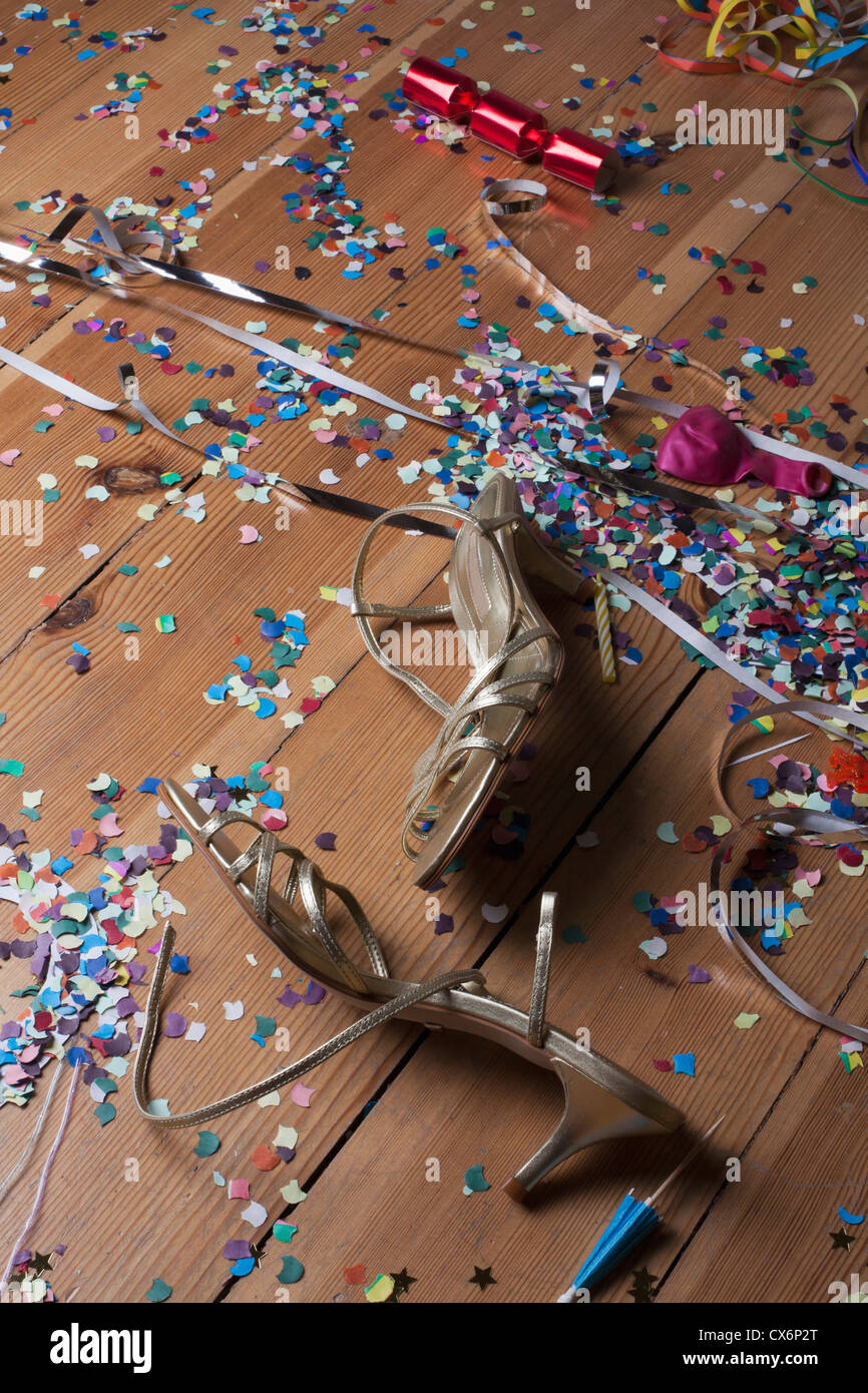 Strappy metallico tacchi, coriandoli e stelle filanti littering un pavimento di legno duro Foto Stock