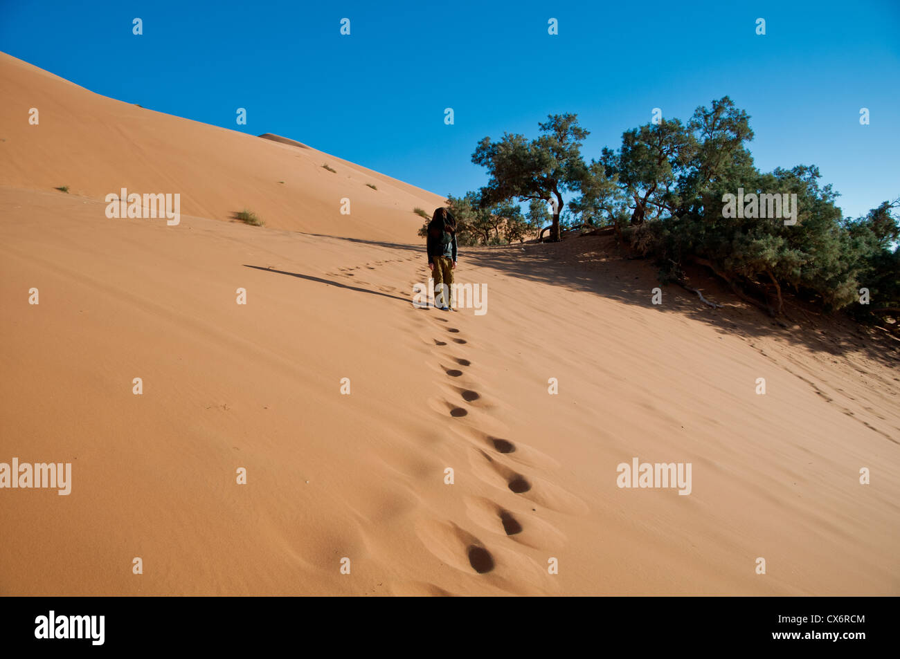 Piedi le tracce in una sahariana duna di sabbia portano a un uomo, con il volto coperto da un foulard nero. Foto Stock