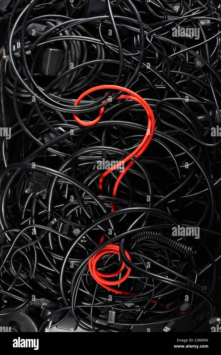 Un unico cavo rosso a forma di punto interrogativo fra un groviglio di nero corde e cavi Foto Stock