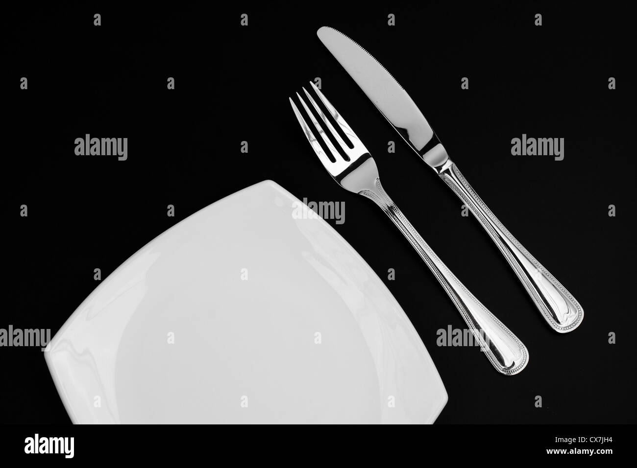 Coltello, quadrato piatto bianco e forcella su sfondo nero Foto Stock