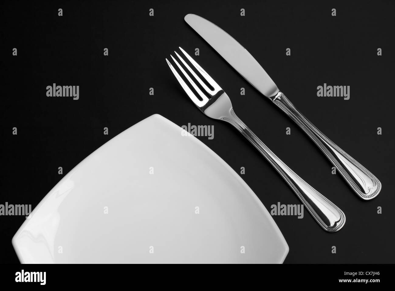 Coltello, quadrato piatto bianco e forcella su sfondo nero Foto Stock