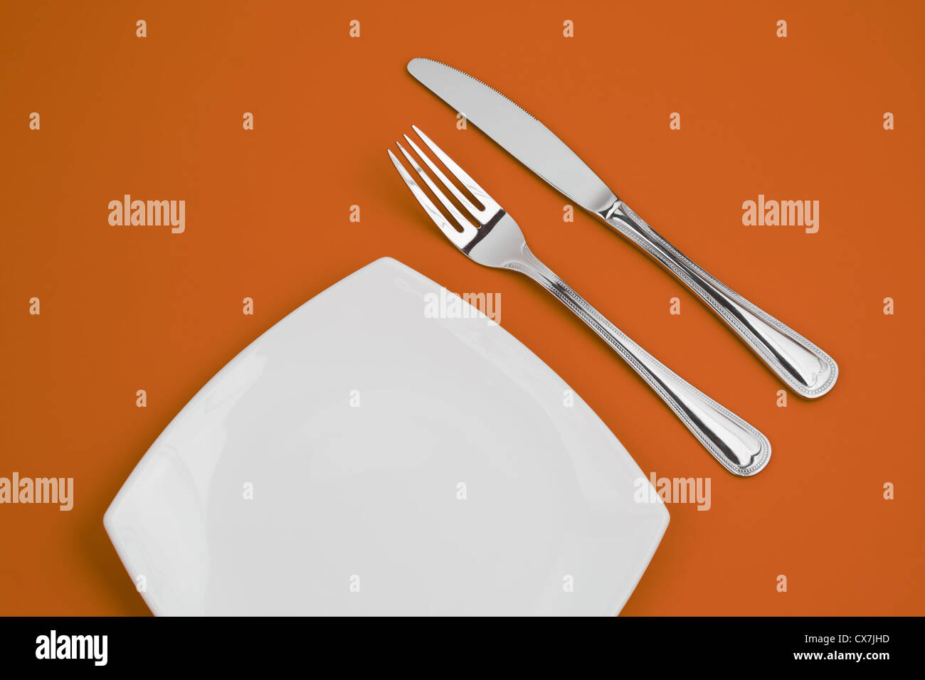 Coltello, quadrato piatto bianco e forcella su sfondo arancione Foto Stock