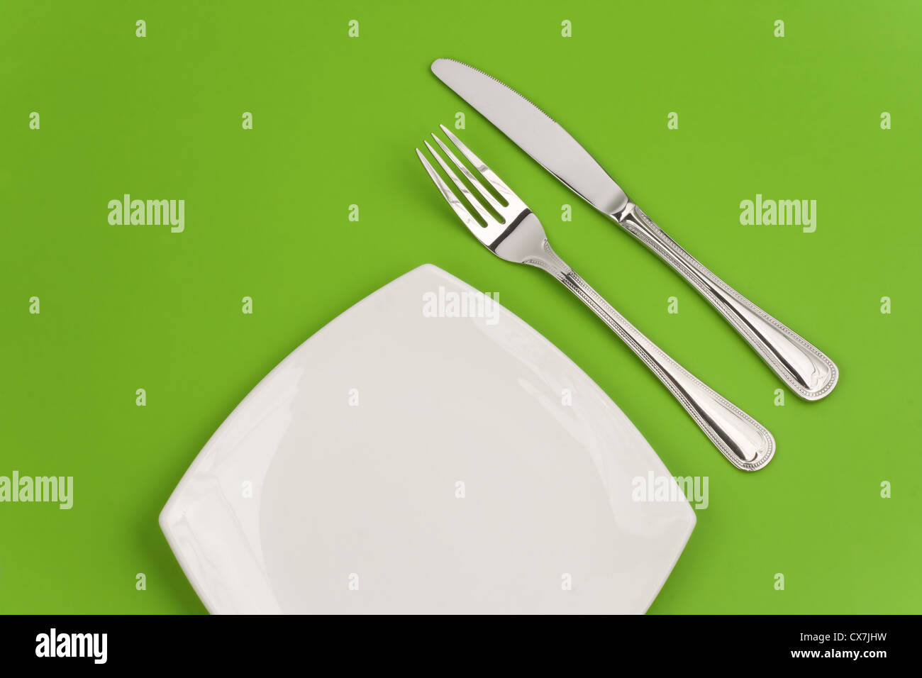 Coltello, quadrato piatto bianco e forcella su sfondo verde Foto Stock