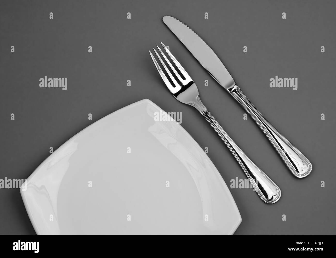 Coltello, quadrato piatto bianco e forcella su sfondo grigio Foto Stock