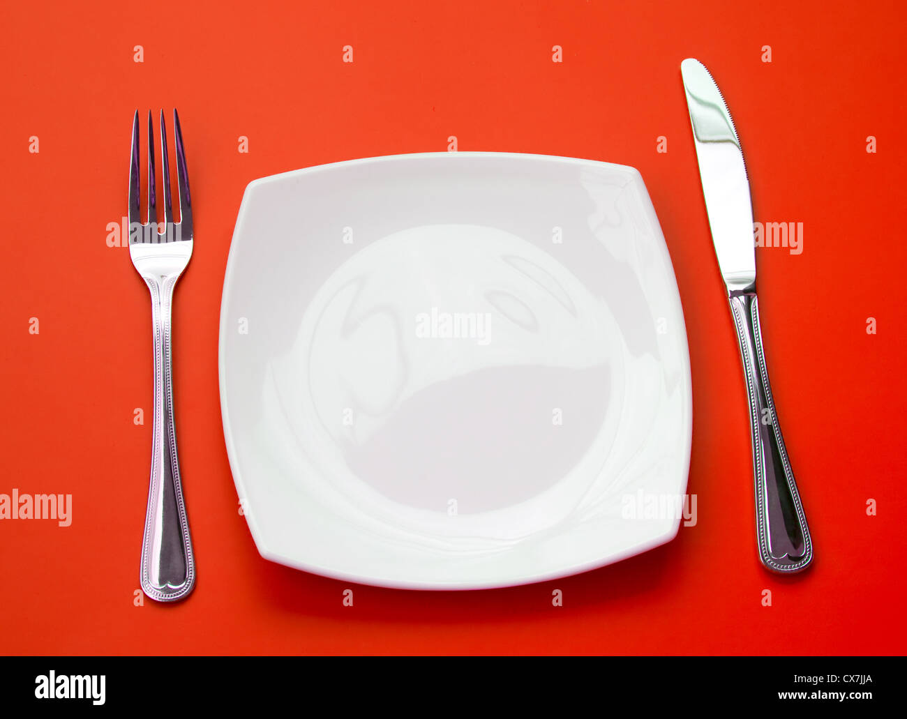 Coltello, quadrato piatto bianco e forcella su sfondo rosso Foto Stock
