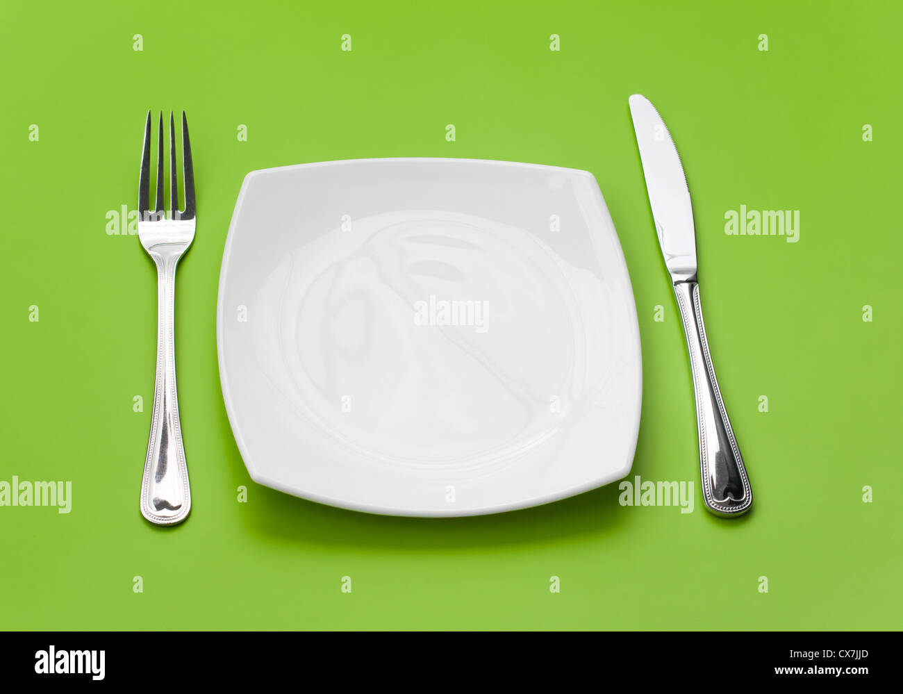 Coltello, quadrato piatto bianco e forcella su sfondo verde Foto Stock