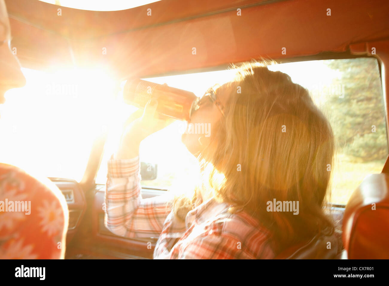 Una donna di bere da un possibile mentre sedendo nel sedile del passeggero di auto d'epoca Foto Stock