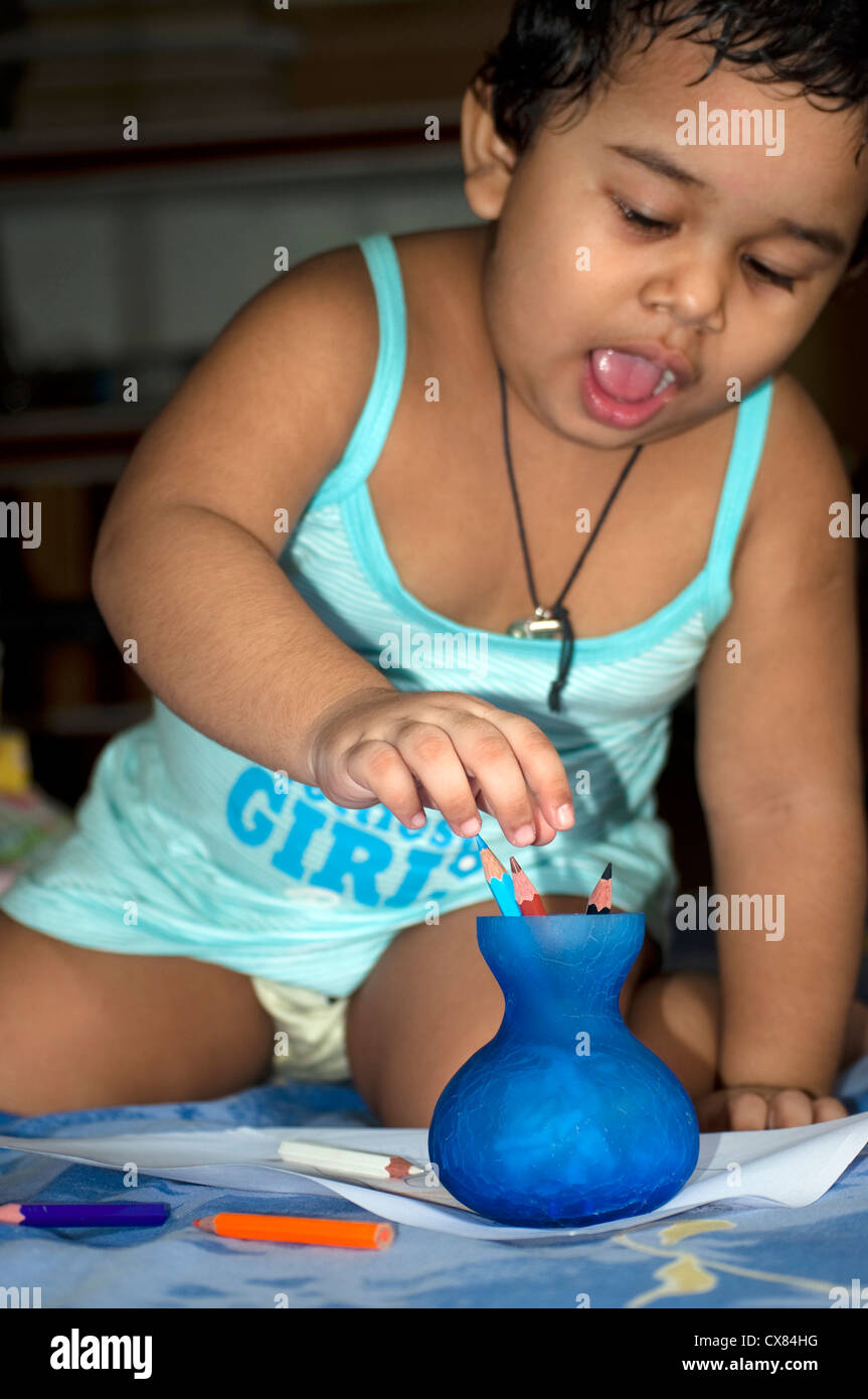 Una ragazza indiana sta giocando con le matite colorate tenute in un piccolo vaso blu Foto Stock