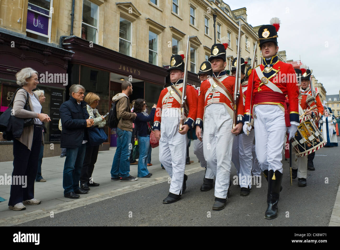 Red rivestire i soldati in uniforme di Regency costume marzo attraverso il centro di Bath all'inizio della Jane Austen Festival Foto Stock