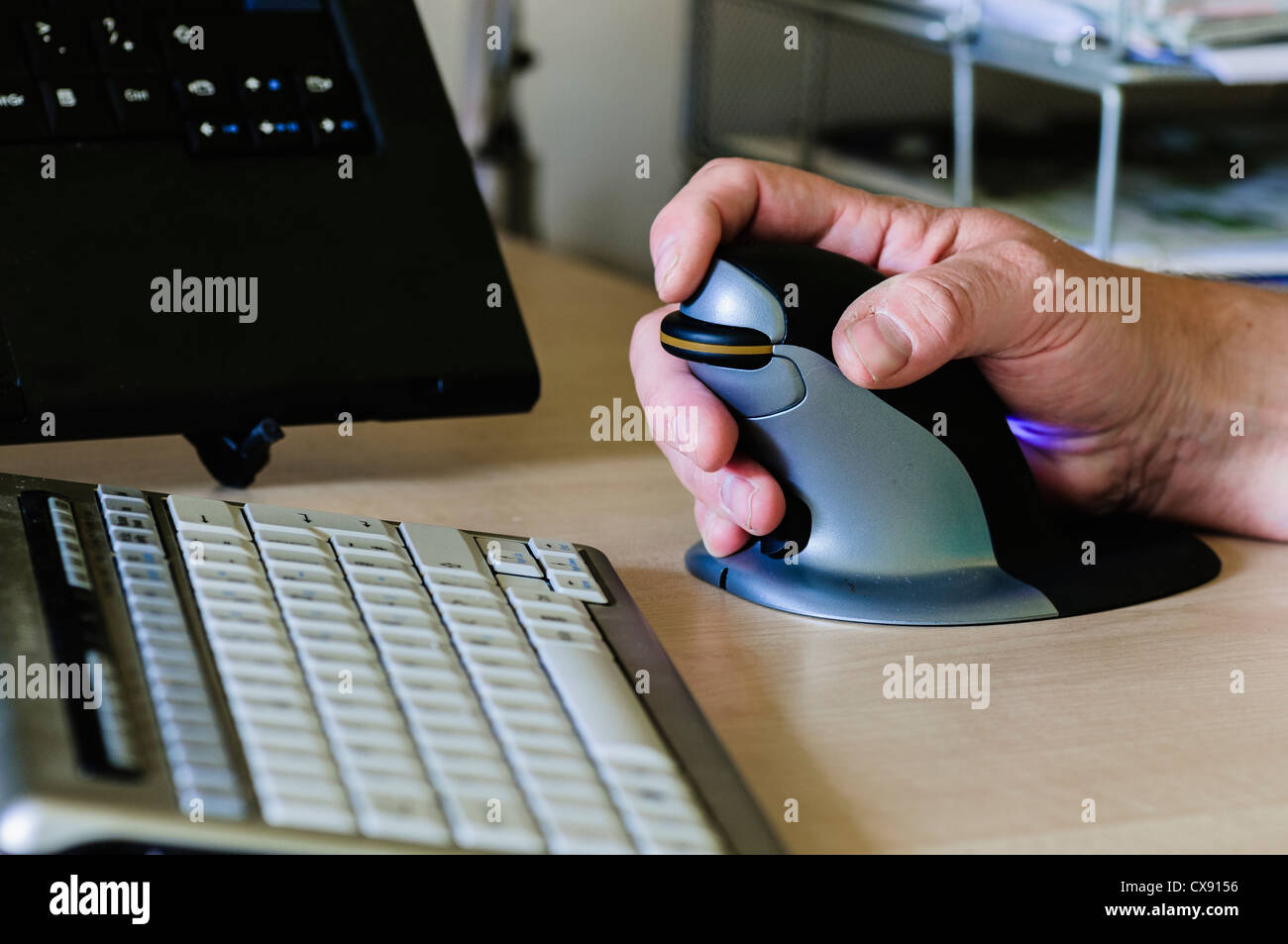L'uomo utilizza un pinguino ergonomica verticale il mouse del computer per le persone con dolori al polso Foto Stock