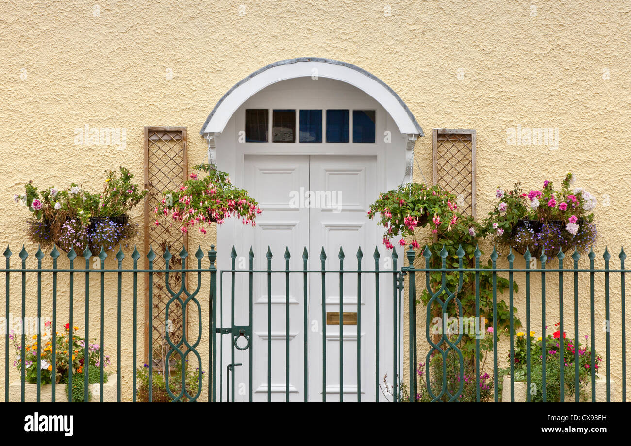 Bianco ornato davanti casa porta con fiori nei cestini appesi Foto Stock