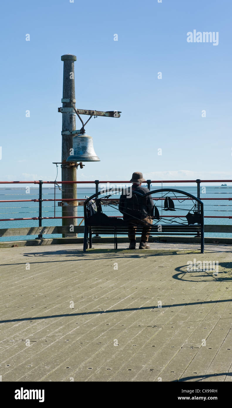 Un uomo seduto da solo su una sede di estremità di un molo. Foto Stock