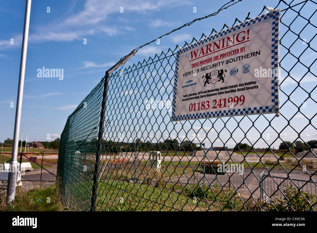 Un sito brownfield in attesa di sviluppo è recintata. Un avviso segnala al pubblico che il sito è protetto da una ditta di sicurezza. Foto Stock